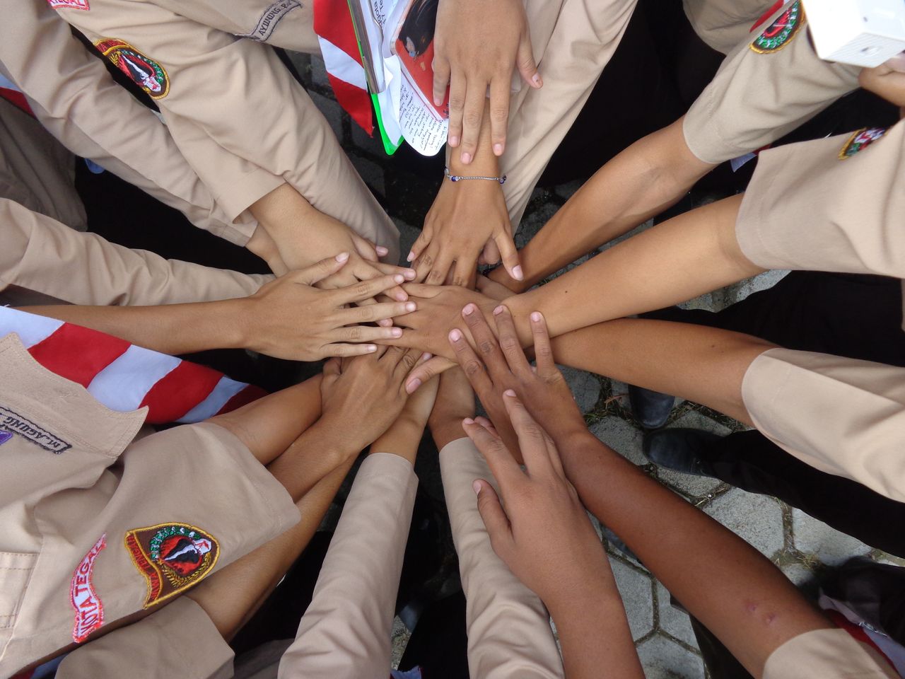 Top view crop anonymous ethnic female servicewomen in military uniforms joining hands while standing on paved street