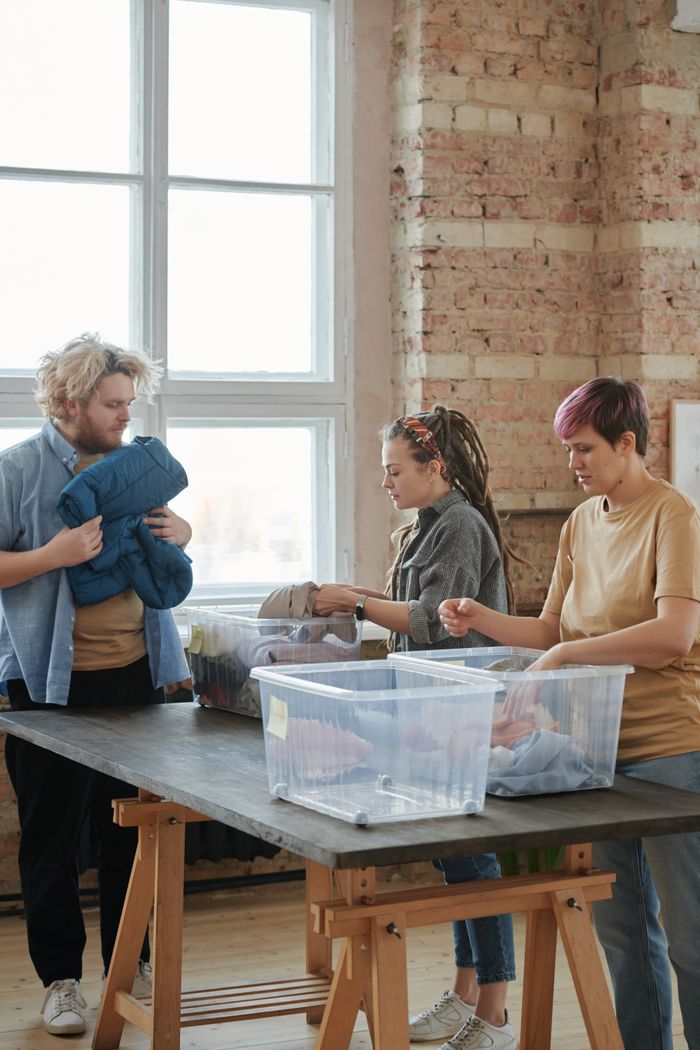 About Three volunteers sorting clothes indoors. Engaged in organizing for charity, teamwork, and community service.