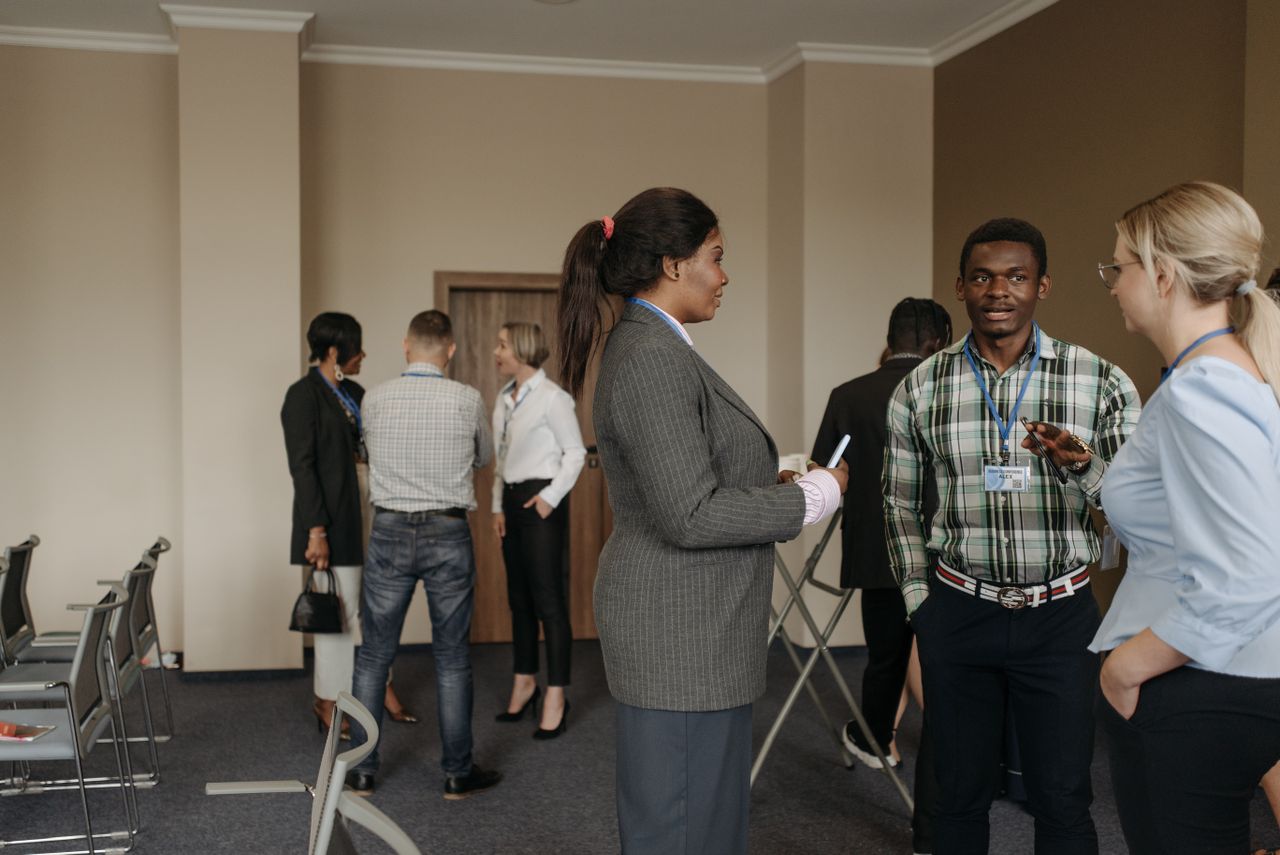 About Professionals engaging in conversation at a diverse business conference with corporate attire indoors.